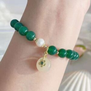 A close-up image of a green quartzite beaded bracelet on a woman's wrist, featuring a natural stone strand with varying shades of green