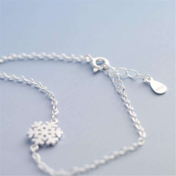 A close-up image of a wrap charm bracelet adorned with delicate snowflake charms, styled on a woman's wrist